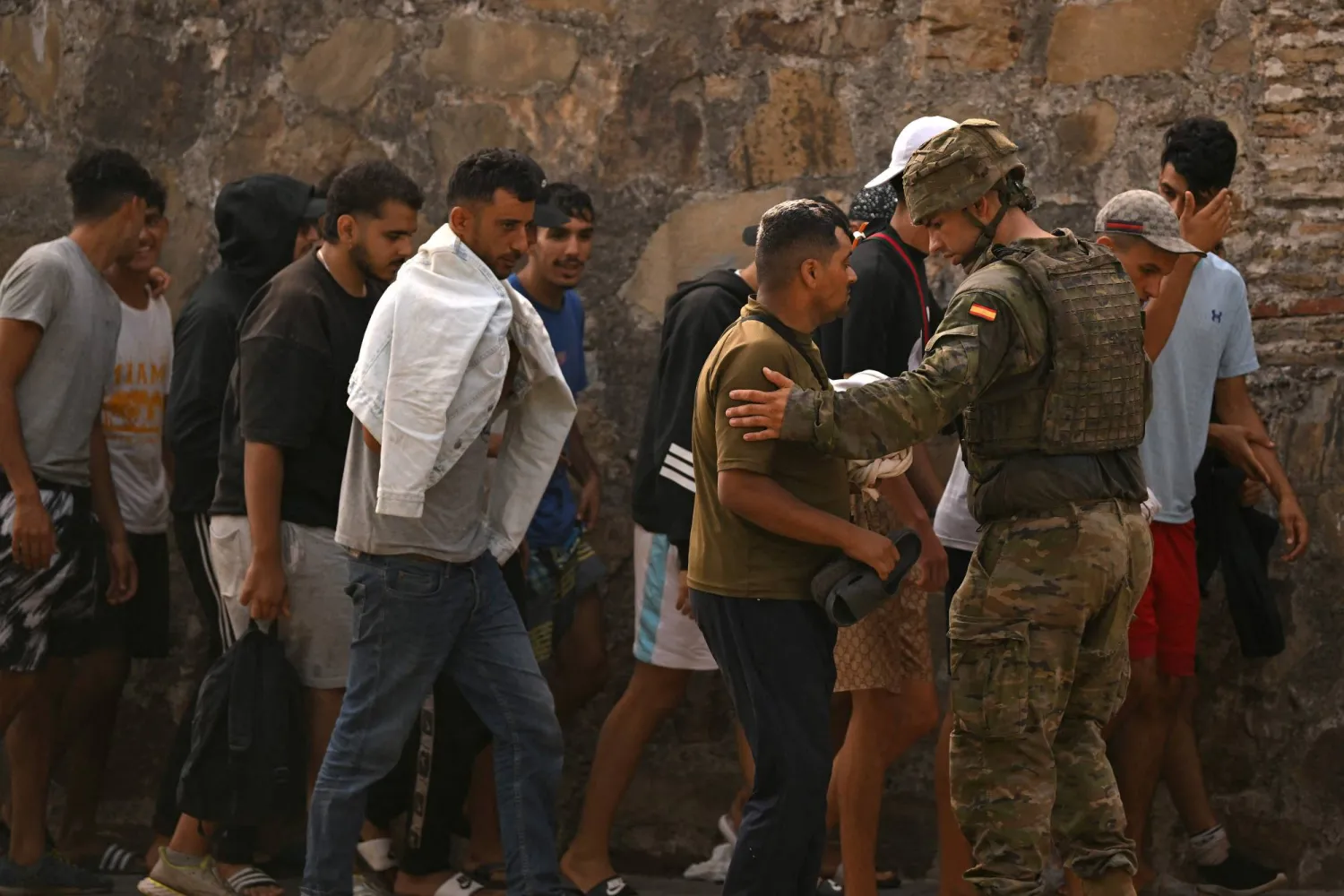 A Spanish soldier escorts a group of young migrants near a stone wall in Ceuta