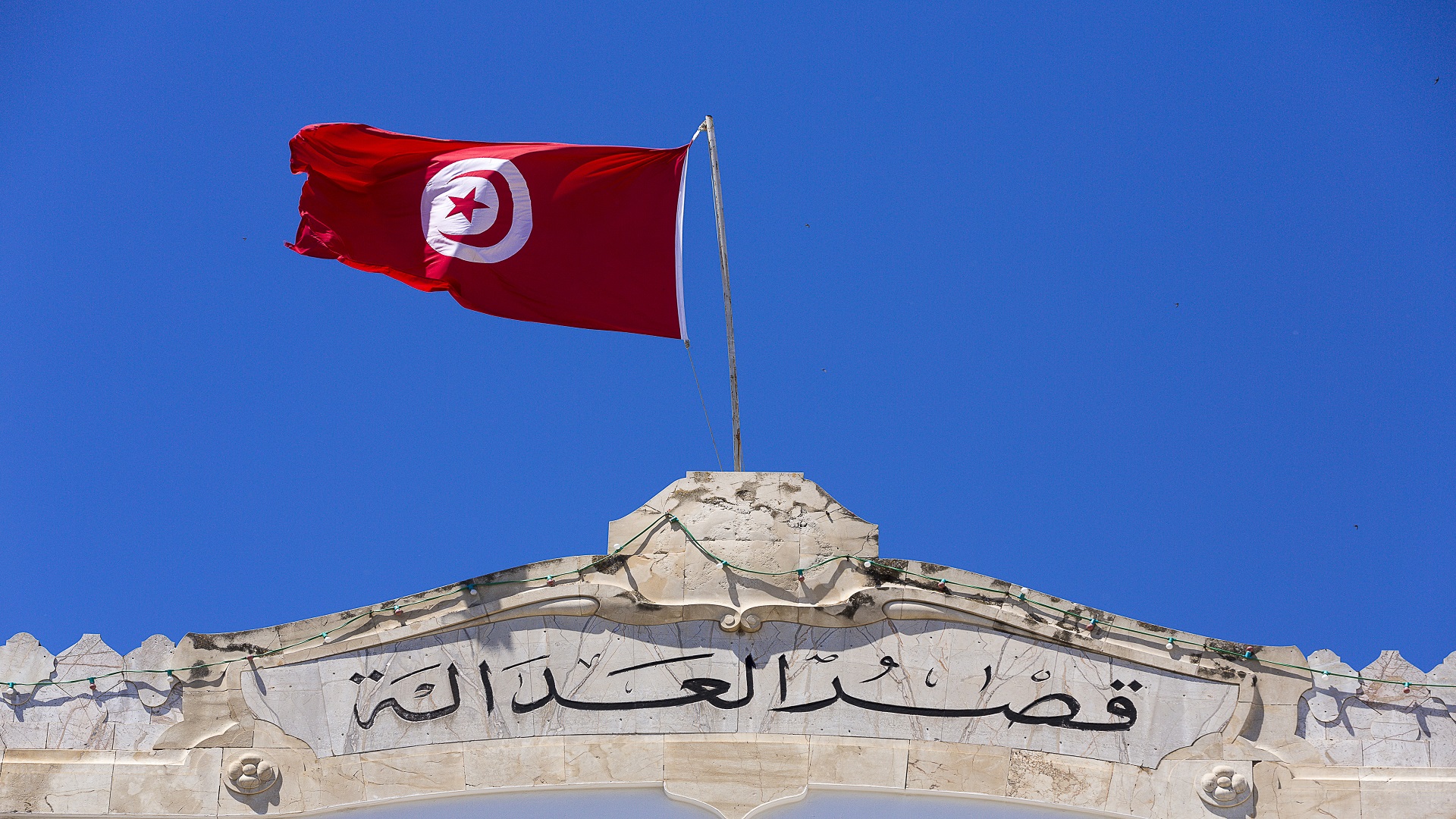 The Tunisian flag flying above a stone facade inscribed "Palace of Justice" in Arabic, file photo