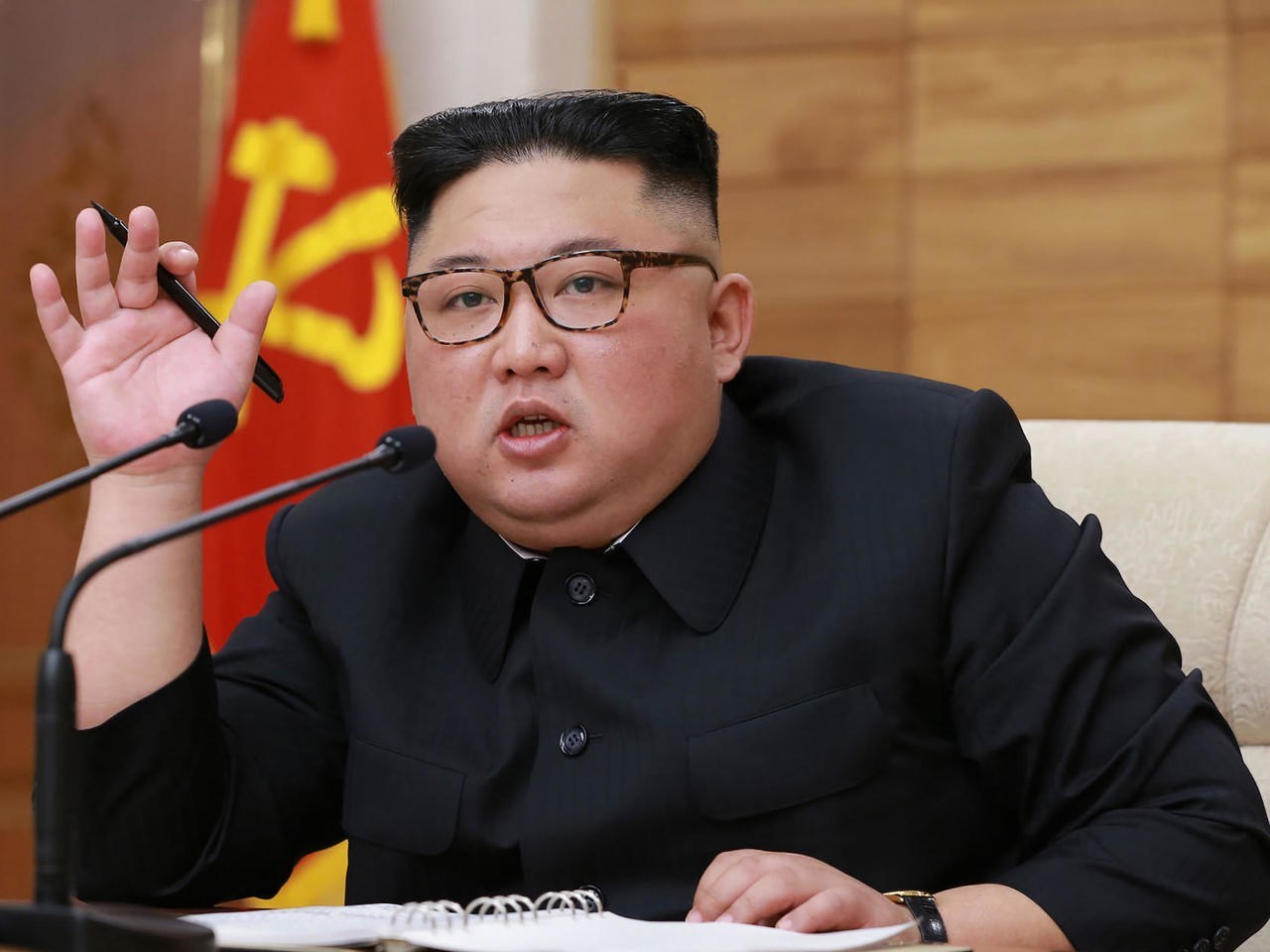 North Korean leader Kim Jong Un speaks behind two microphones holding a pen, file photo