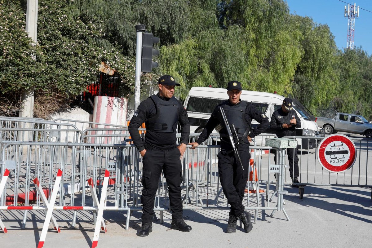 Two Tunisian security officers in black uniforms in front of metal barriers and a police stop sign, file photo