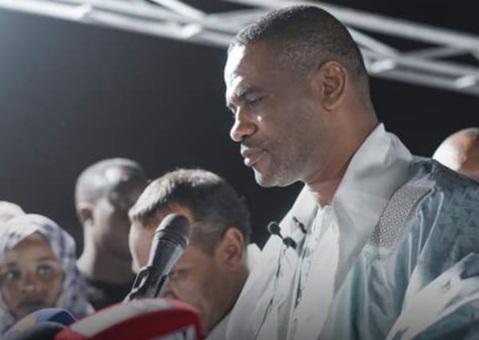 A man speaks into a microphone at an evening event