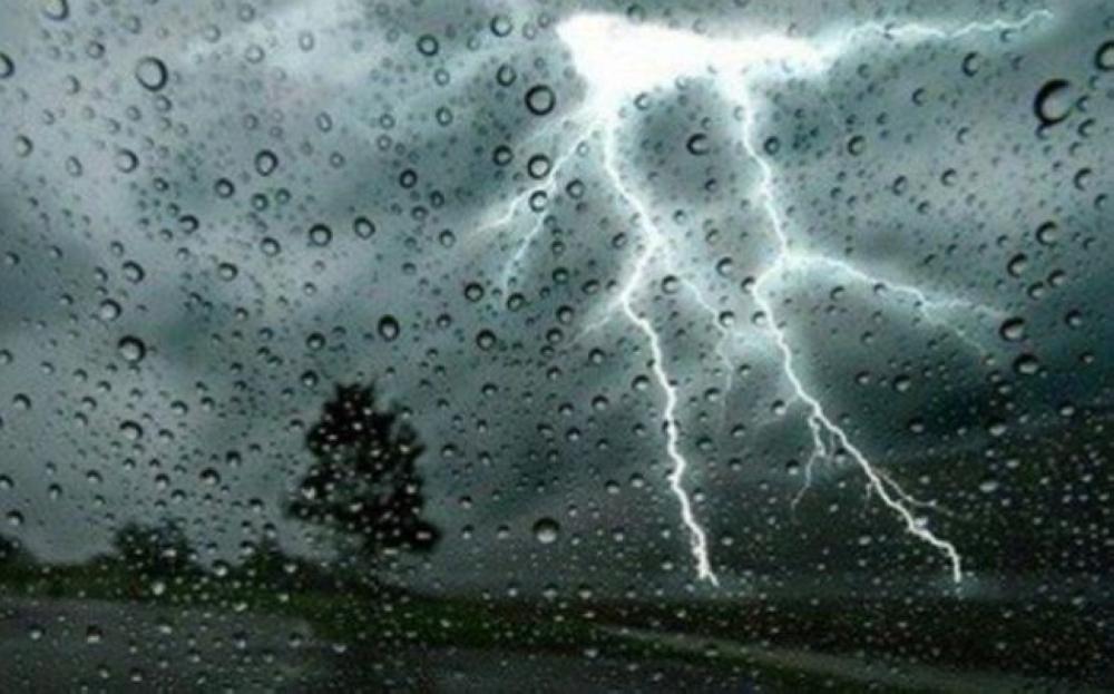 Lightning in a cloudy sky behind glass covered in raindrops, illustrative image