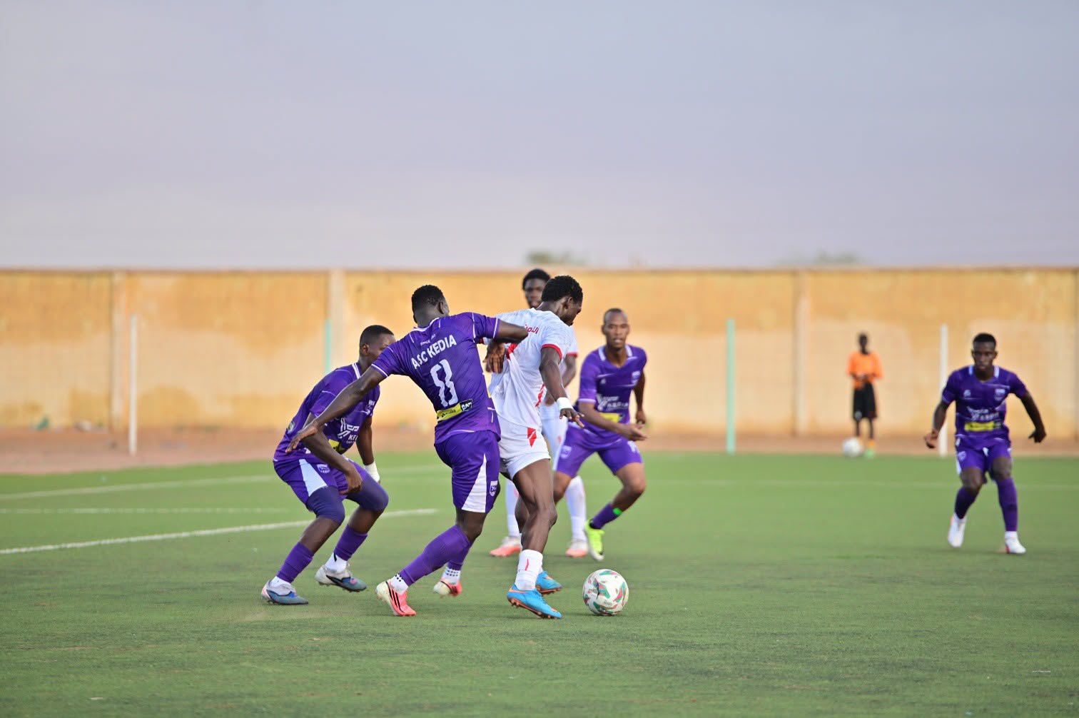Players contest the ball during a match on a grass pitch