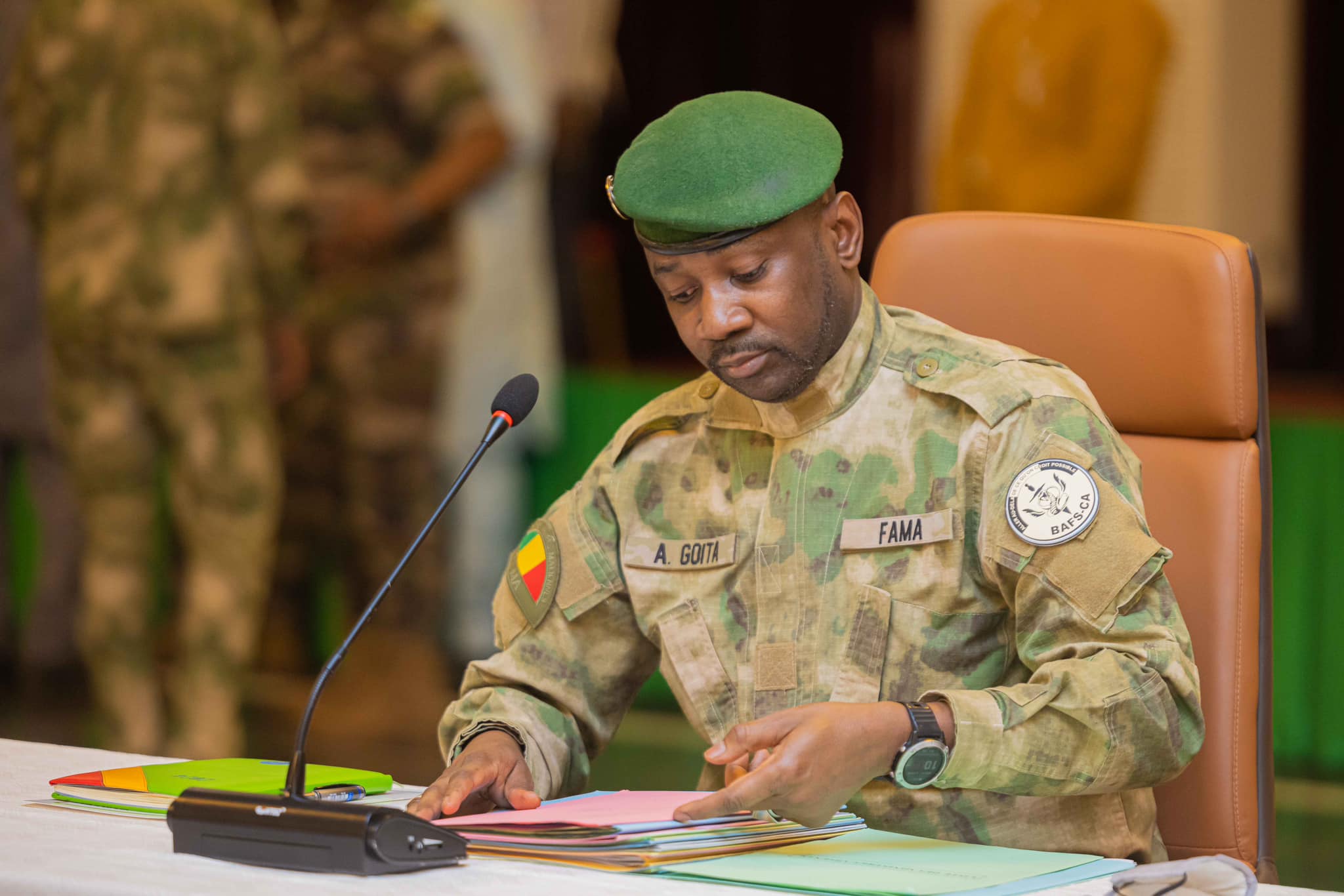 Assimi Goita in military uniform and a green beret, leafing through files in front of a microphone, file photo