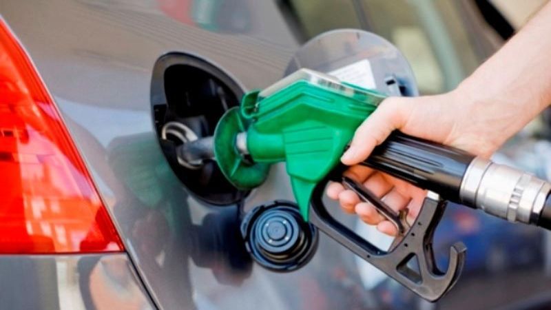 Hand holding a green fuel pump nozzle in the tank of a grey car, file photo