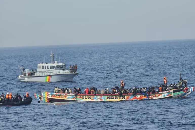 A white patrol boat and an inflatable beside a colourful canoe crowded with migrants at sea, file photo