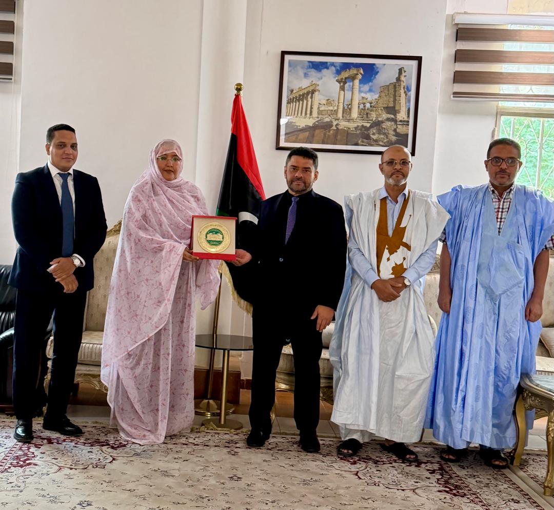 Parliamentarians present a plaque to the ambassador in front of the Libyan flag