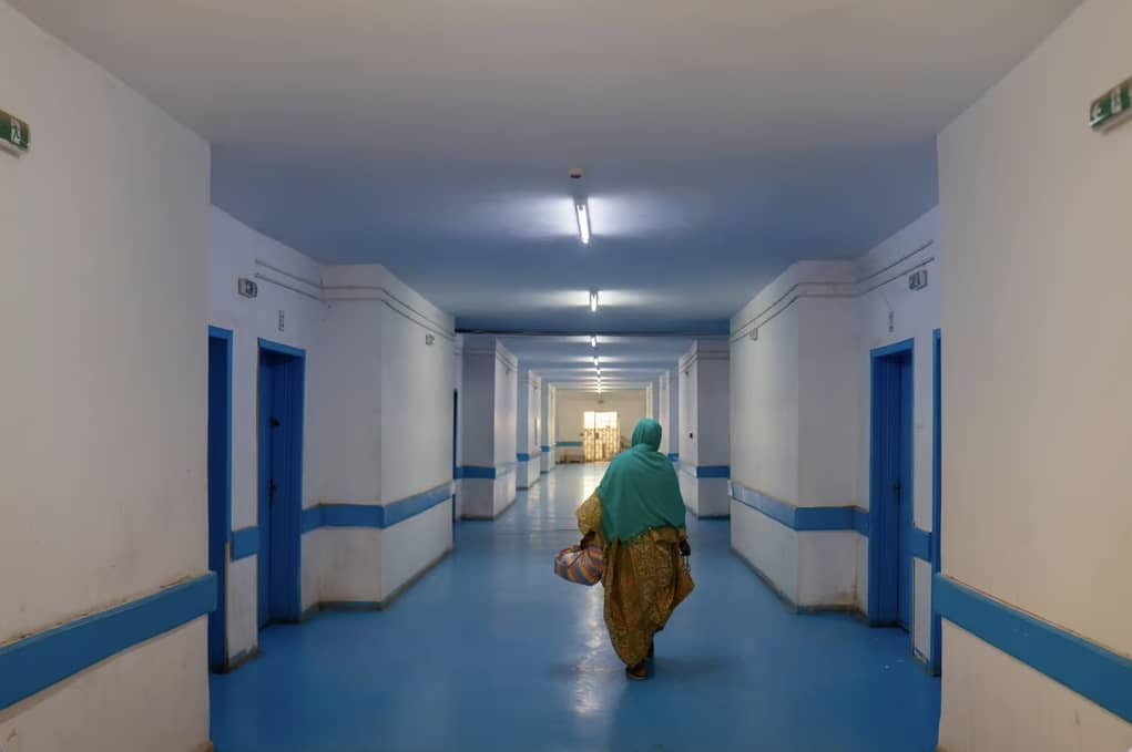 A woman walks down a hospital corridor with white and blue walls