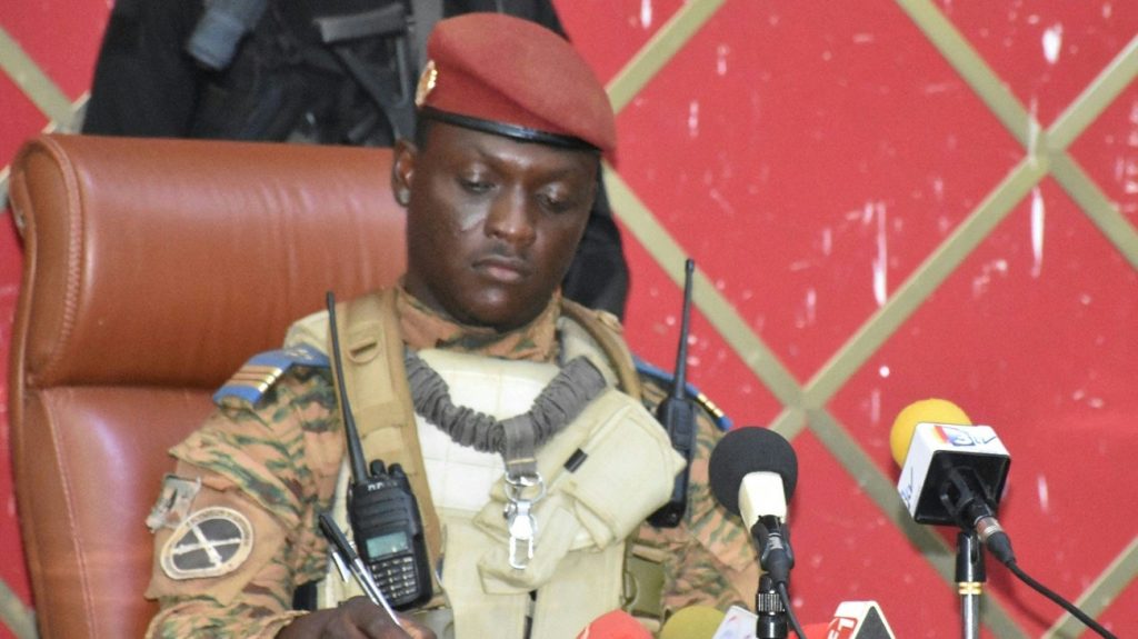 Captain Ibrahim Traore in fatigues and a red beret signing a document in front of microphones