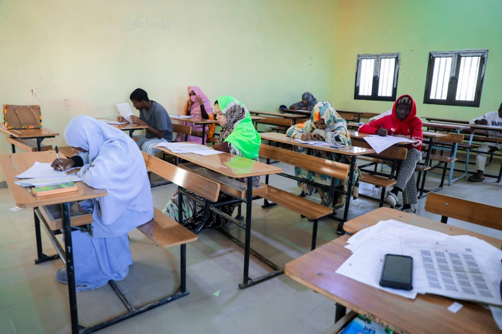 Students seated at desks in an exam room writing on papers