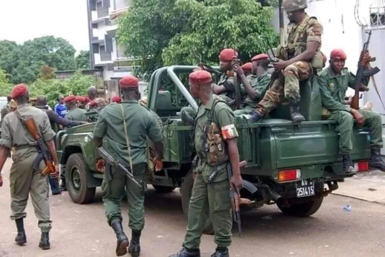 Armed Guinean soldiers in red berets around a green military vehicle in a street, file photo