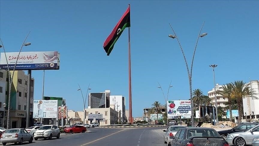 A tall flagpole flying the Libyan flag at the centre of a roundabout surrounded by cars, buildings and billboards, file photo