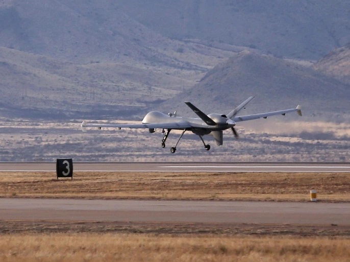 A grey military drone flying low over a runway surrounded by hills, illustrative file image