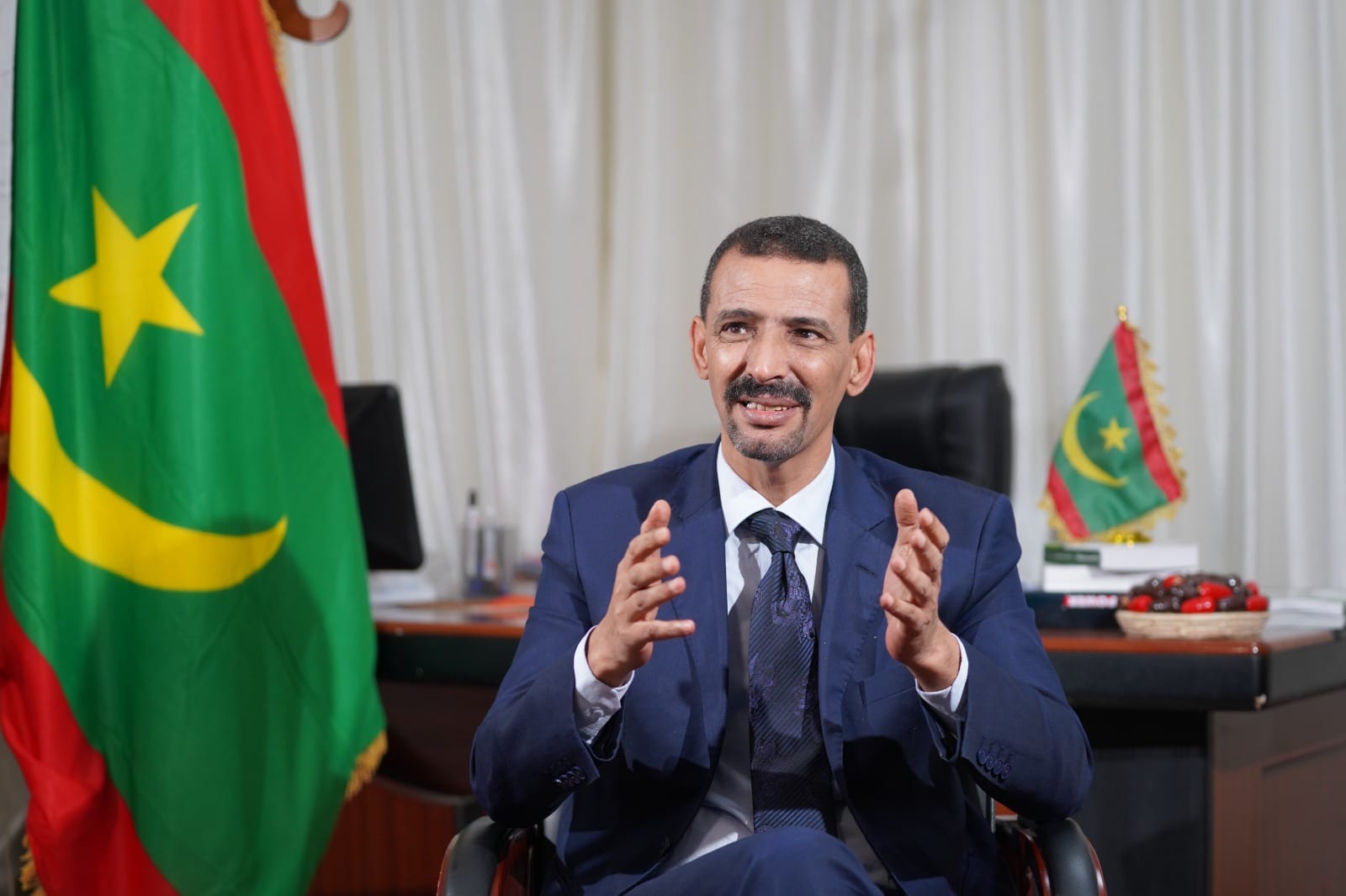 El Houssein Ould Meddou speaking in his office in front of the Mauritanian flag