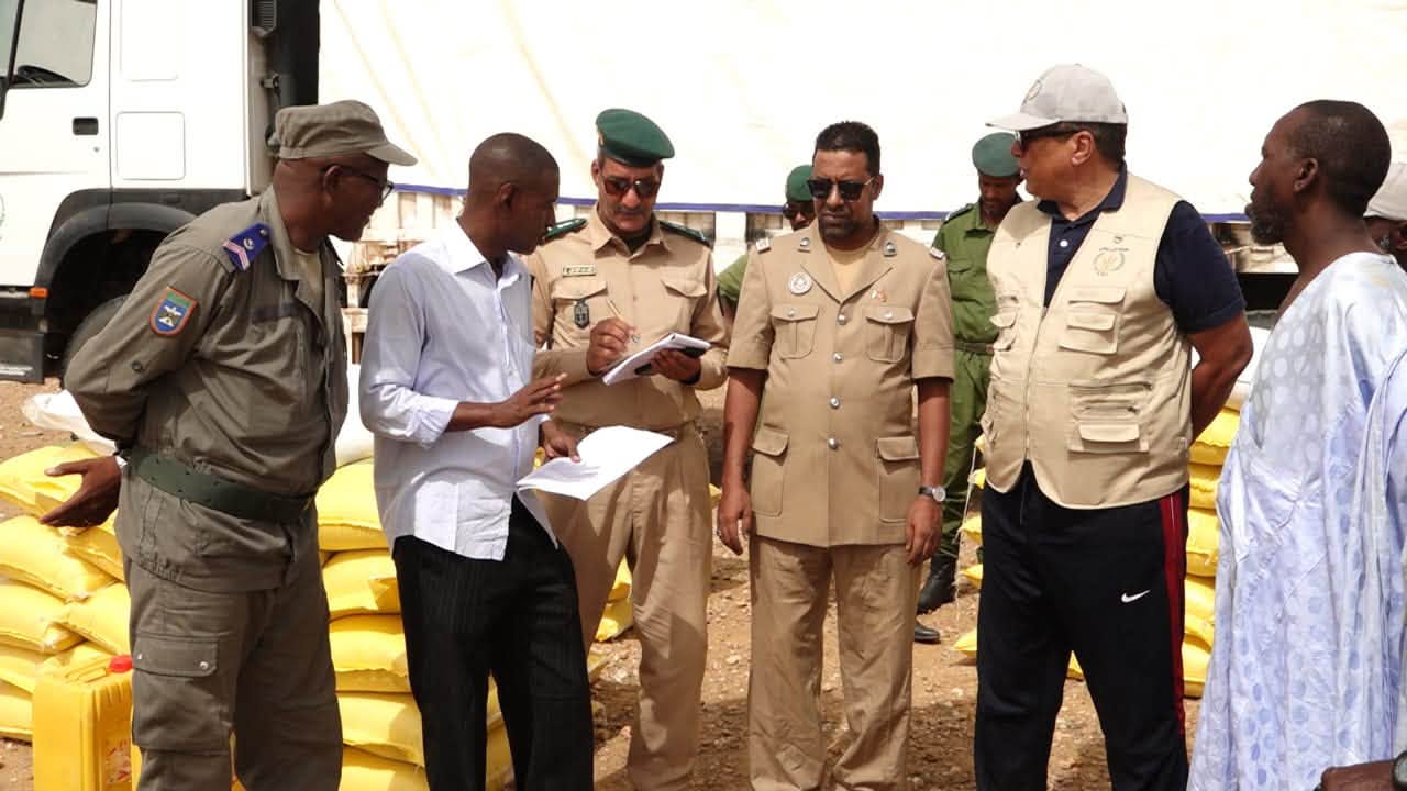 Administrative officials and security officers check lists in front of sacks of food aid and a truck