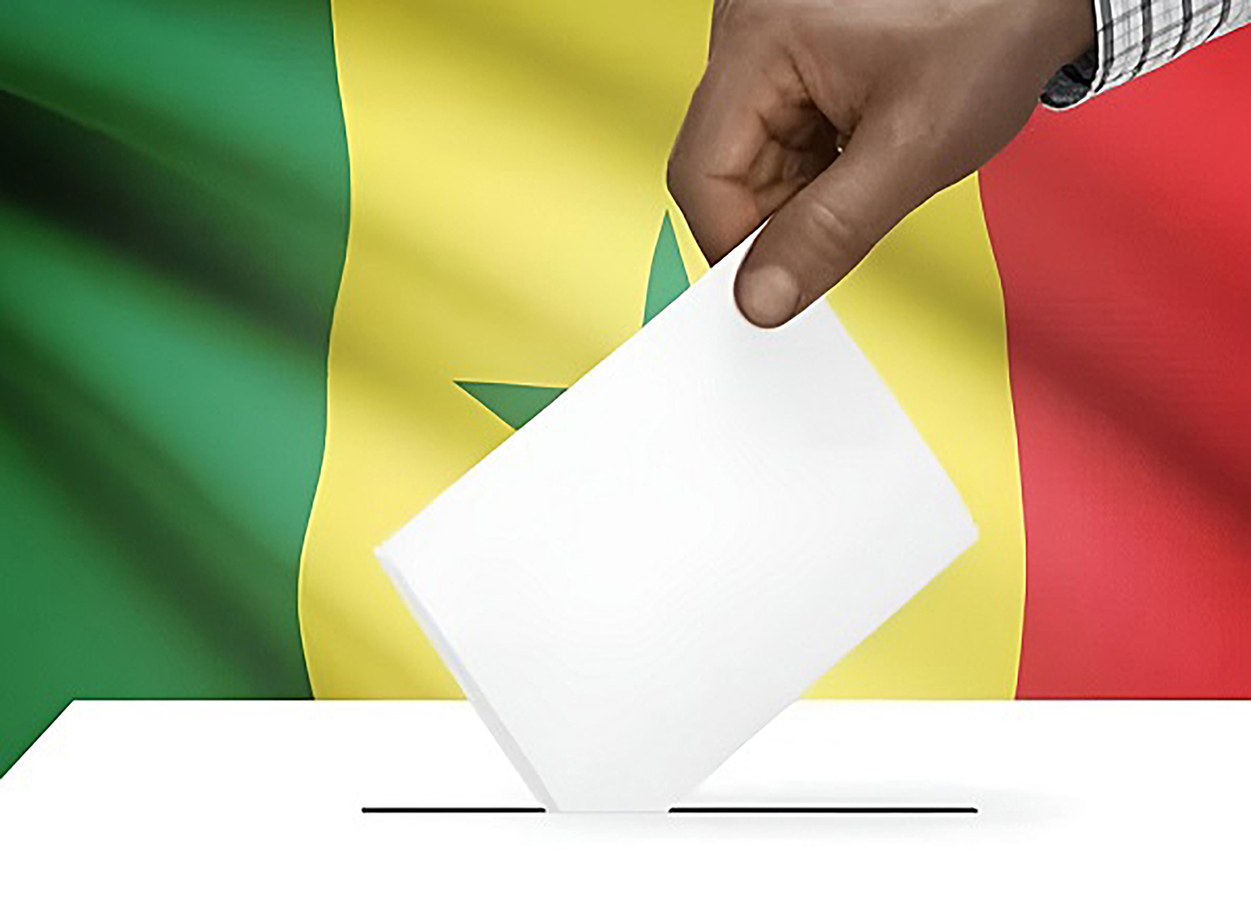 A hand drops a ballot into a box in front of the Senegalese flag