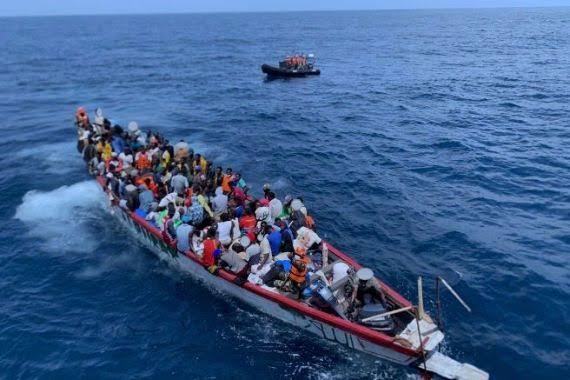 A boat crowded with migrants at sea, near a rescue vessel