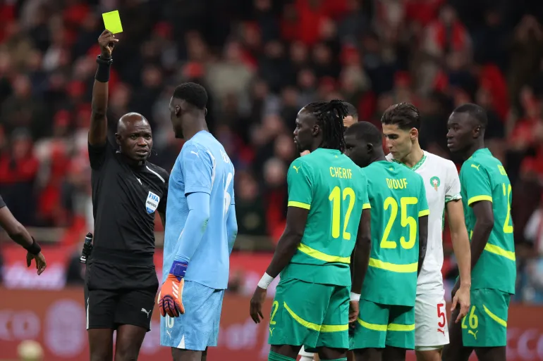 A referee shows a yellow card in front of players from Senegal and Morocco