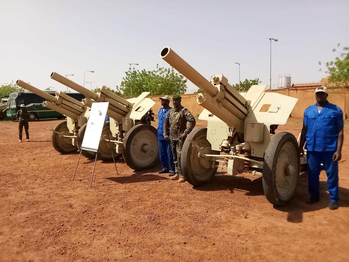Three field guns on red laterite ground next to a soldier and workers in blue overalls, file photo