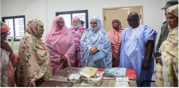 Women in traditional veils and a man in a blue boubou standing around a table covered with fabrics